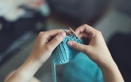 Image of a pair of hands knitting with blue yarn.