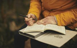 Person holding a pen and writing in a notebook.