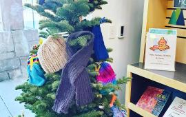 Tree decorated with hats, scarves, and mittens.