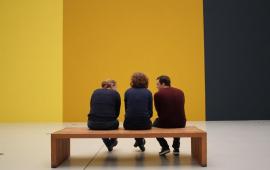 Three people sitting on a bench viewing art.