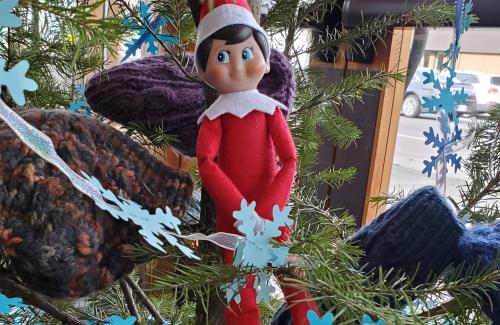 Toy elf sitting in a decorated holiday tree.