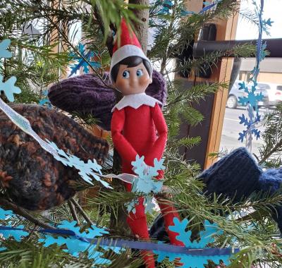 Toy elf sitting in a decorated holiday tree.