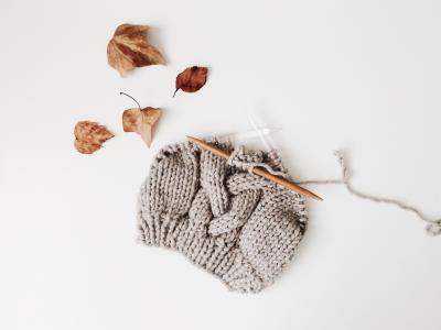 Grey knit hat with knitting needles sticking out of it.