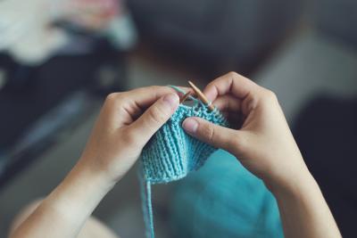 Image of a pair of hands knitting with blue yarn.