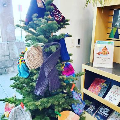 Tree decorated with hats, scarves, and mittens.