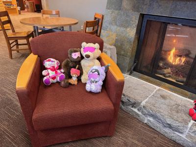 Stuffed animals sitting in a chair together by a fireplace.